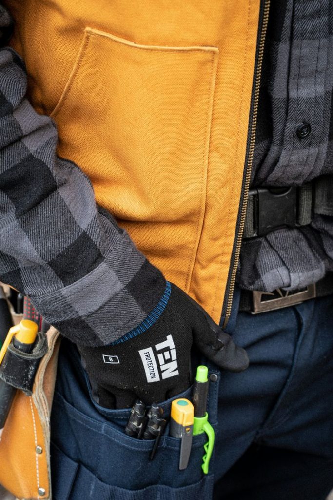 Close-up of a construction worker’s tool belt and gloved hand, showing various tools and workwear details.